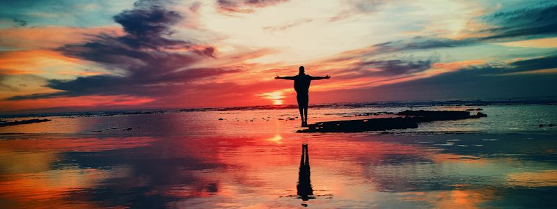 silhouette of person standing on rock surrounded by body of water