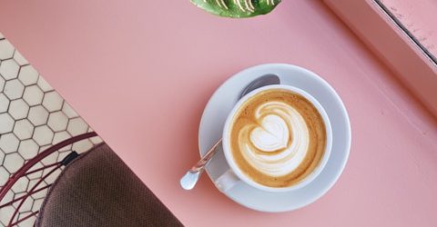 cup of coffee on saucer with teaspoon on pink tabletop