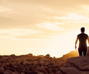 man walking on gray rocks under yellow sky during daytime