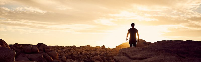 man walking on gray rocks under yellow sky during daytime